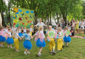 W kole tańczą dzieci przebrane za motyle. W tle rodzice oglądający przedstawienie.